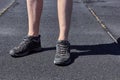 The legs of a man in short shorts and black sneakers. Black and gray asphalt background. Legs of young man in black sneakers.