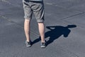 The legs of a man in short shorts and black sneakers. Black and gray asphalt background. Legs of young man in black sneakers.