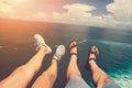 Legs of man in sandals and woman in sport shoes sitting above blue ocean