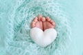 Legs newborn baby close up on a blue background with a toy in the form of a heart