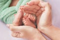 Legs of a newborn baby in gentle hands of mother on a lilac background