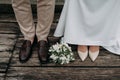 Legs of newlyweds on wooden background. stylish shoes of bride and groom outdoors. bridal bouquet on brige close up Royalty Free Stock Photo