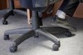 The legs of an office clerk or dispatcher on duty sitting on a pneumatic chair with wheels. Concept of office furniture and its