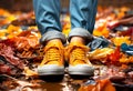 Legs in old sneakers standing on ground with carpet of yellow leaves in fall. Autumn season concept Royalty Free Stock Photo