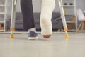 Legs part of young man with broken leg in cast walking with crutches at home