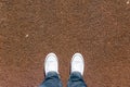 Legs on red tartan sports field with two shoes, personal perspective from above