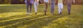 Legs of several men and women holding hands walking along green grass in summer park Royalty Free Stock Photo