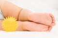 The legs of a sleeping baby on a white blanket and a yellow rubber ball for massage nearby