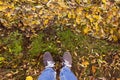 Legs in sport shoes standing on yellow autumn leaves in grass. Feet shoes walking in fall nature Royalty Free Stock Photo