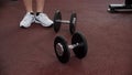 Legs of sportsman is walking near the dumbbells in gym on floor during the rest between reps.