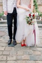 Legs of the stylish wedding couple, groom in black shoes and bride in red heels shoes with a luxury wedding dress Royalty Free Stock Photo