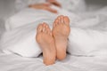 Legs of tired caucasian millennial female lies on bed under white blanket, sleep at night, enjoy rest, relax
