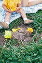 Legs of a toddler sitting on a blanket on a green lawn next to toys