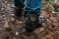 The legs of tourist in hiking boots on a walk in the fall are walking along a muddy wet trail. Active recreation concept