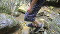 Legs of traveler moves from stone to stone on mountain stream in forest