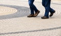 Legs of two men walking on concentric circles pavement