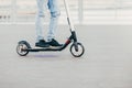 Legs of unknown male in black sneakers and jeans rides on electric scooter over urban asphalt, enjoys sunny day. People and leisur