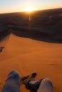 Legs of unrecognizable man from the top of a dune at sunrise, in Erg Chigaga, Morocco