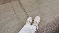 Legs in white jeans and white sneakers on gray pavement tiles. The concept of travel, traveler, buying new shoes Royalty Free Stock Photo