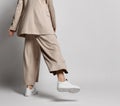 Legs of woman in beige business smart casual pantsuit, sneakers walking over light. Stylish business female wear