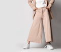 Legs of woman in beige business smart casual suit and sneakers standing over light. Stylish business female wear