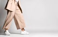 Legs of woman in beige business smart casual suit and sneakers walking over light. Stylish business female wear