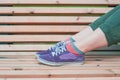 Legs of woman in green pants and purple sneaker on the bench