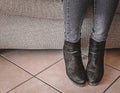 The legs of a woman sitting on the sofa, dressed in semi-boots and jeans. Modesty. Soft grey and beige colors