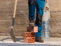 Legs of worker with foot on bricks and shovel in hand vertically in construction