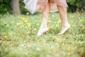 Legs of young barefoot women wearing pink dress standing on one leg on green grass with yellow flowers, close up Royalty Free Stock Photo