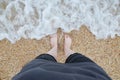 Legs of a young girl in shorts on a sandy beach near the foaming sea waves Royalty Free Stock Photo