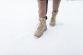 Legs of a young girl in trendy pants with brown winter boots walk on snow. Winter collection of fashionable shoes. Close-up.