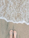 Legs of a young woman with a pedicure in slates on a sandy beach near the sea. The wave is coming. Copy space. Top down Royalty Free Stock Photo