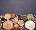 Legumes, lentils, chickpeas and beans assortment in various bowls on black stone background, top view with copy space