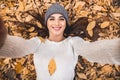 Leisure in the autumnal park. Top view of beautiful young woman lies on autumn leaves and making selfie Royalty Free Stock Photo