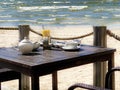 Leisure cafe on beach at sea ,summer holiday restaurant table with cup coffee tea and glass of white wine blue sky sunlight beams Royalty Free Stock Photo