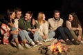 Group of friends sitting at camp fire on beach Royalty Free Stock Photo