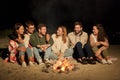 Group of friends sitting at camp fire on beach Royalty Free Stock Photo