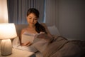 Leisure and people concept - young woman reading book in bed at night home Royalty Free Stock Photo