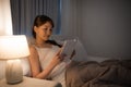 Leisure and people concept - young woman reading book in bed at night home Royalty Free Stock Photo