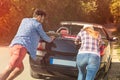 Leisure, road trip, travel and people concept - happy friends pushing broken cabriolet car along country road Royalty Free Stock Photo