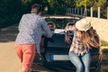 Leisure, road trip, travel and people concept - happy friends pushing broken cabriolet car along country road Royalty Free Stock Photo