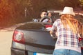 Leisure, road trip, travel and people concept - happy friends pushing broken cabriolet car along country road Royalty Free Stock Photo