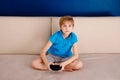 Leisure time, children, technology and people concept - little blonde boy with gamepad playing video game at home Royalty Free Stock Photo