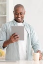 Leisure time. Happy black man reading e-book on digital tablet and drinking coffee in kitchen Royalty Free Stock Photo