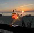 Glass of juice with ice water splash and sun beam flares on wooden table top sunset at sea in beach restaurant view in pink sky a Royalty Free Stock Photo