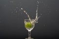 Lemon falling into a glass of transparent water causing splashes upwards. Isolated on gray background Royalty Free Stock Photo