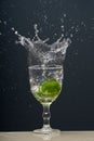 Lemon falling into a glass of transparent water causing splashes upwards. Isolated on gray background Royalty Free Stock Photo