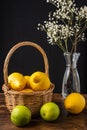 Lemon and lime close-up, basket with lemons, bottle with white flowers, with selective focus, on wooden table and black background Royalty Free Stock Photo