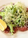 Lemon slice beef carpaccio, salad, parmesan and sauce, on a white plate